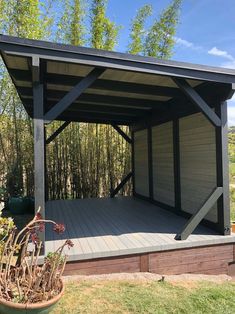 a wooden deck with a metal roof in the middle of some grass and trees behind it