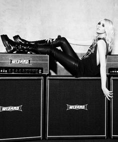 a woman laying on top of two amps in front of a wall with guitars