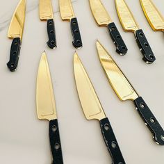 several knives are lined up on a table with black handles and gold blades in the middle