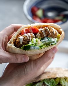 a hand holding a pita filled with meatballs and veggies