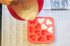 someone is making heart shaped ice cubes out of plastic trays on top of newspaper pages