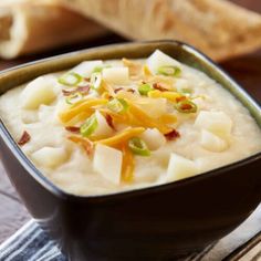 a close up of a bowl of food on a table with bread in the background