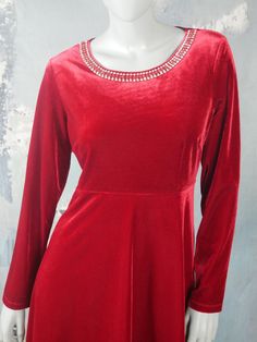 This red velvet dress has a round neckline, with a shimmering band of faux red coral gemstone bars and diamanté crystals in the front. The European vintage slip-on dress has long sleeves, a fitted waistline, and a semi-flared skirt. Bust = 42 inches (106.68cm) Shoulders = 17 inches (43.18cm) Waist = 36 inches (91.44cm) Hips = 45 inches (114.3cm) Dress Length = 37 inches (93.98cm) Size: 14 US, 18 UK Material: 90% polyester, 10% elastan --- CONDITION --- This stunning red velvet dress is vintage, Red Velvet Dress For Holidays, Holiday Red Velvet Dress, Red Fitted Velvet Dress For Winter, Fitted Red Velvet Winter Dress, Red Velvet Long Sleeve Evening Dress, Festive Red Velvet Dress, Red Fitted Velvet Dress With Long Sleeves, Fitted Red Velvet Long Sleeve Dress, Red Long Sleeve Velvet Dress For Party