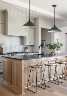 a kitchen with an island and bar stools next to the counter top, along with two hanging lights