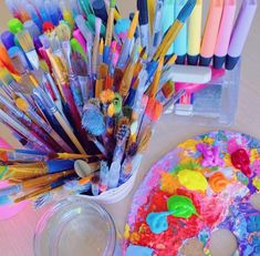 there are many different colored paints and brushes in the container next to each other on the table