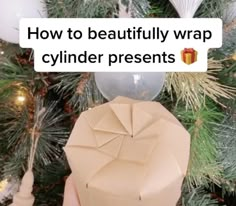 someone is holding a present in front of a christmas tree with the caption how to beautifully wrap cylinder presents