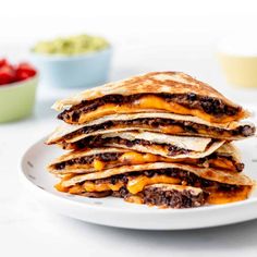 a stack of quesadillas sitting on top of a white plate next to a bowl of salsa