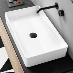 a white sink sitting on top of a black counter next to a wall mounted faucet