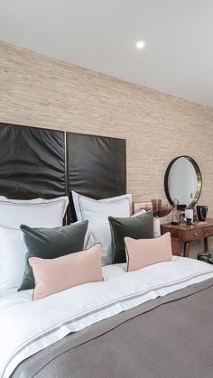 a large bed with white sheets and pillows in a bedroom next to a mirror on the wall