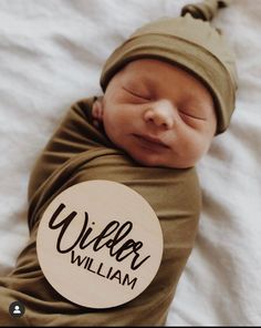 a newborn baby wrapped in a brown wrap and holding a wooden sign that says, villier william