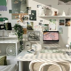 a white desk topped with a laptop computer next to a wall covered in pictures and plants