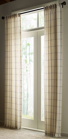 an open window with white curtains in front of it and a rug on the floor