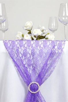 a purple table runner with white roses and wine glasses