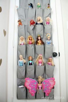 barbie dolls are sitting on the back of a gray bag that is hanging from a wall