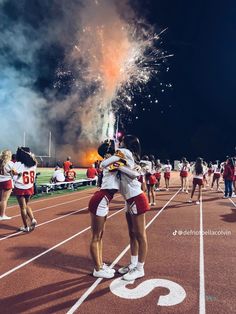 cheerleaders huddle around on the sidelines as fireworks go off in the background