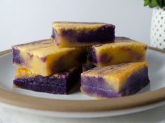 four pieces of purple and yellow cake on a plate next to a potted plant