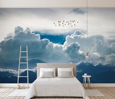 a bed sitting under a cloudy sky with birds flying in the air above it and a ladder leaning against the wall