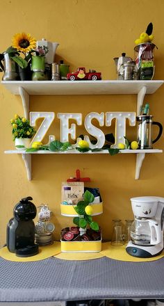 a yellow table topped with two shelves filled with cups and saucers next to a coffee maker