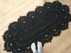 someone is standing on the floor next to a black crocheted rug with white shoes