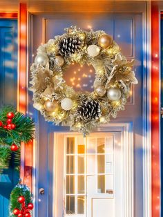 a christmas wreath hanging on the front door of a house decorated with pine cones and ornaments