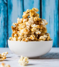 a white bowl filled with caramel popcorn on top of a wooden table next to blue boards