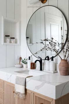 a bathroom sink with a round mirror above it and some flowers in a vase on the counter