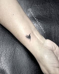 a small black bird tattoo on the wrist