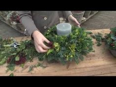 someone is making a wreath out of greenery and candlesticks on a wooden table