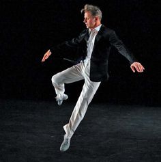 a man in white pants and a black jacket is dancing with his legs spread out