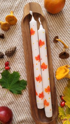 two white candles sitting on top of a wooden tray next to an orange and some leaves