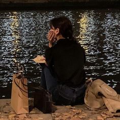 a woman sitting on the edge of a body of water holding her hands to her face