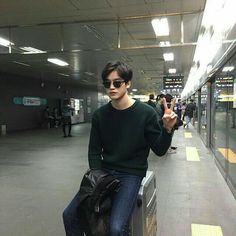 a young man sitting on top of a metal box in an airport terminal holding his hand up