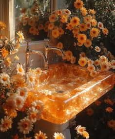 an orange sink surrounded by yellow flowers in front of a window with the sun shining on it