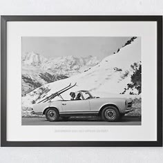 a black and white photo of a car parked in the snow with mountains behind it