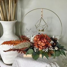 an arrangement of flowers and plants in front of a white vase with a gold geometric decoration