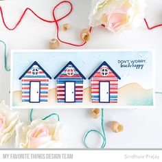 a card with three beach huts on it next to some flowers and twine spools