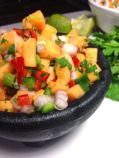 a black bowl filled with pineapple salsa next to cilantro