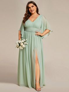 a woman in a long green dress with a slited leg and large cleavage is posing for the camera