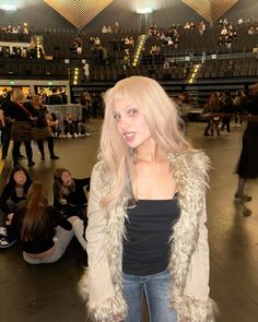 a woman with long blonde hair standing in front of an audience wearing jeans and a fur coat