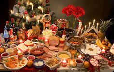 a table filled with lots of food next to a christmas tree covered in candles and decorations