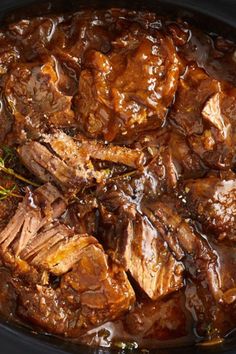 meat and gravy in a crock pot with rosemary sprigs on top