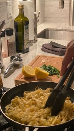 someone is cooking pasta in a skillet on the kitchen counter with lemons and parsley