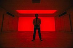 a man standing in an empty room with red light coming from the ceiling and his hands on his hips