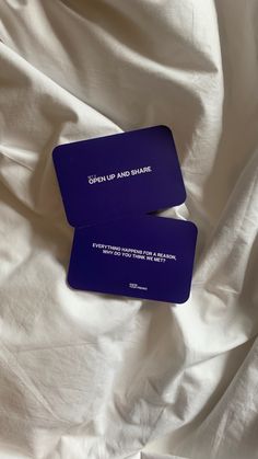 two purple business cards sitting on top of a white bed sheet with the words open up and share