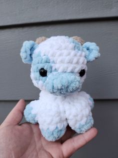 a hand holding a small blue and white crocheted stuffed animal with black eyes