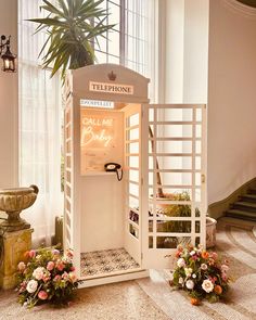 an old fashioned phone booth with flowers in the foreground and stairs leading up to it