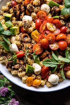 a white bowl filled with pasta salad topped with tomatoes and mozzarella cheeses