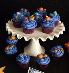 cupcakes with blue frosting and space decorations on a cake platter, surrounded by small toys