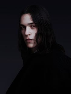 a man with long hair wearing a black sweater and dark background is looking at the camera