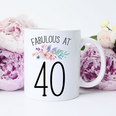 a white coffee mug with the words better late than ugly on it next to pink flowers